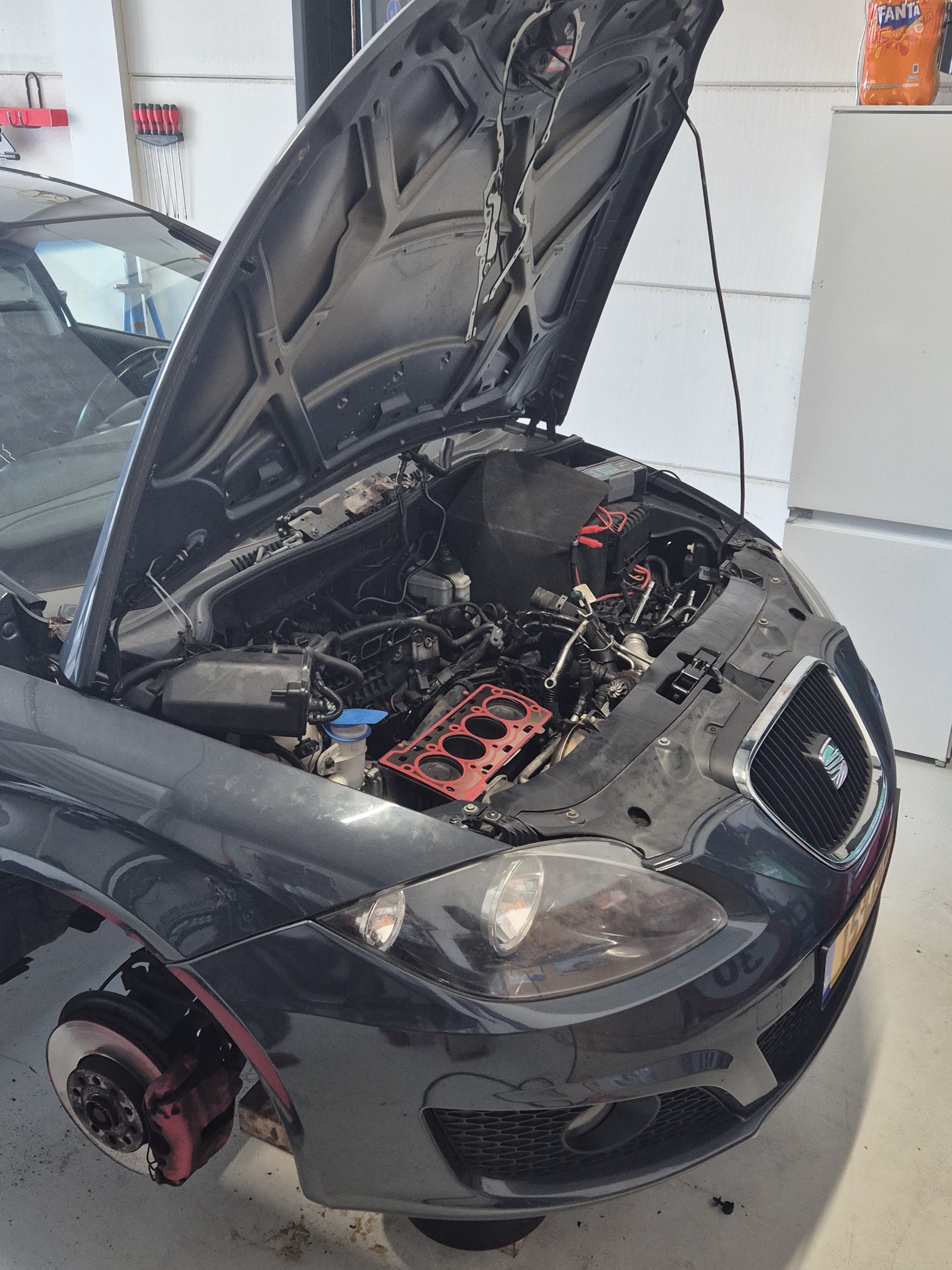 Een donkere auto met geopende motorkap en een gedemonteerde motor in de werkplaats